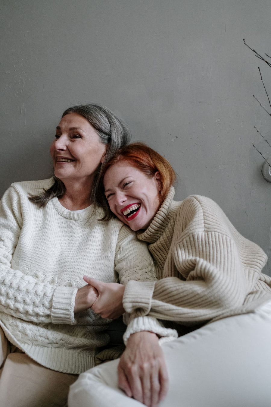 Grey-haired mother and her grown daughter laughing together in cream knitwear